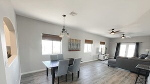 A spacious living room with a dining area, a sofa, ceiling fans, and large windows. - Centrally Located River Home with Mountain Views! (Fort Mohave)