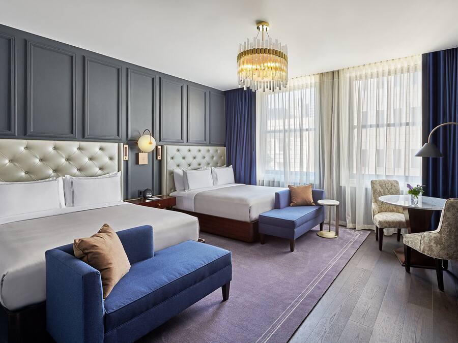 A hotel room with two beds, a blue sofa, a round table, and a chandelier.