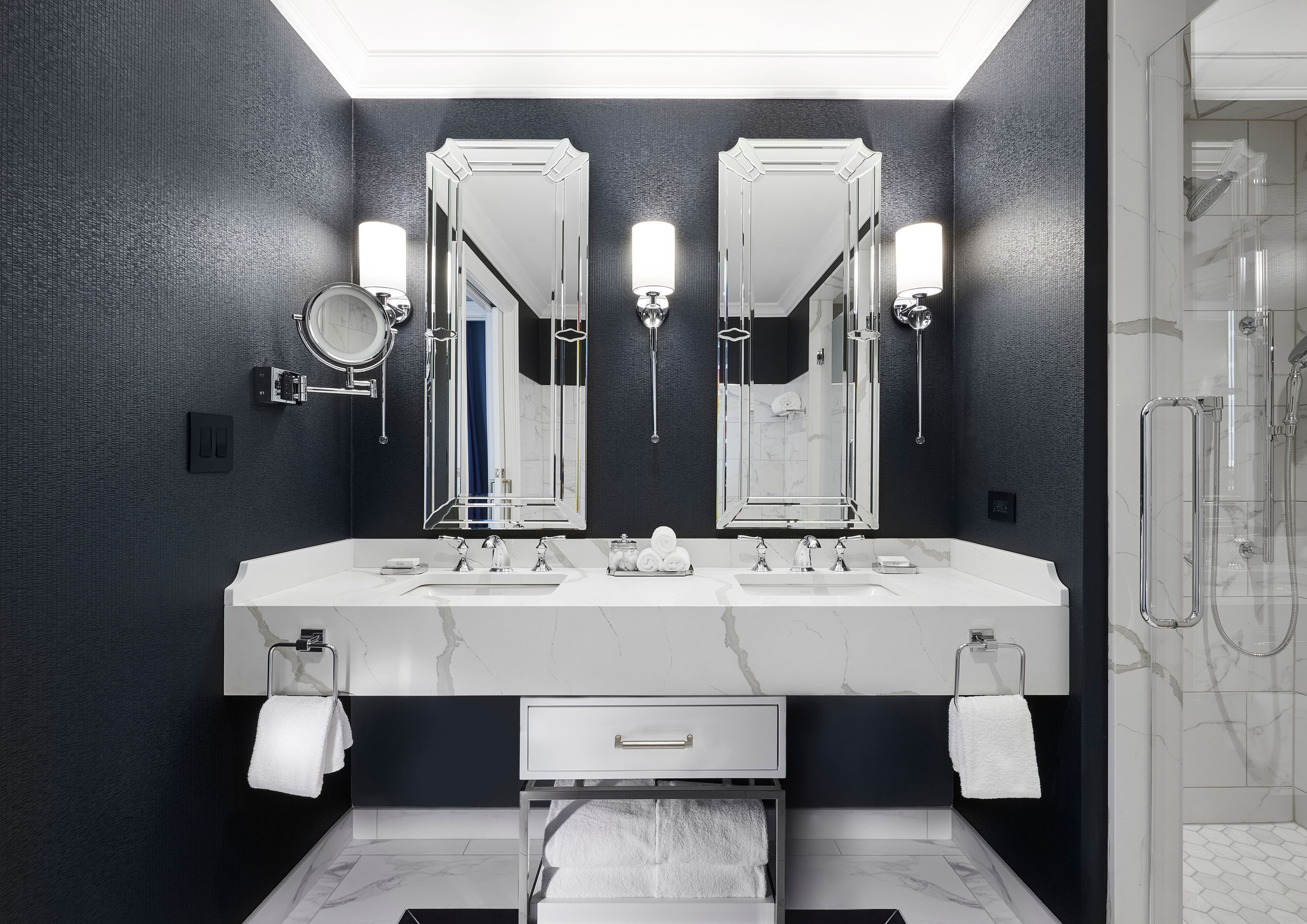 Ein modernes Badezimmer mit dunklen Wänden, zwei großen Spiegeln, einer weißen Waschtischkonsole mit zwei Waschbecken und einer gläsernen Duschkabine.