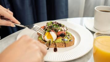 A breakfast plate with avocado toast, a poached egg, and greens, a cup of coffee, and a glass of orange juice on a table.