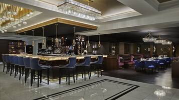 A bar area with a long counter, multiple bar stools, and hanging crystal chandeliers.