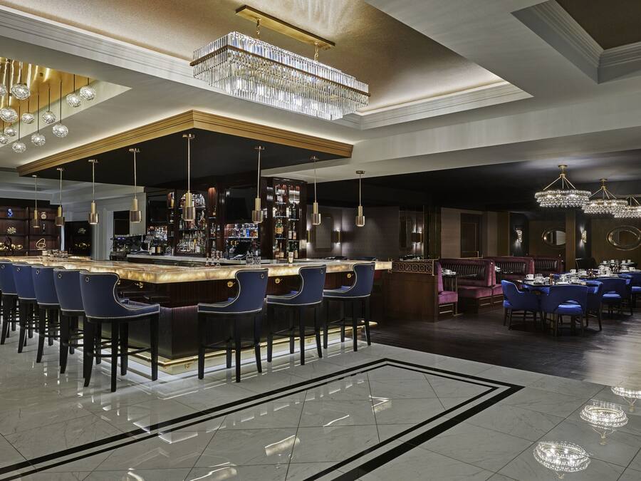 A bar area with a long counter, multiple bar stools, and hanging crystal chandeliers.