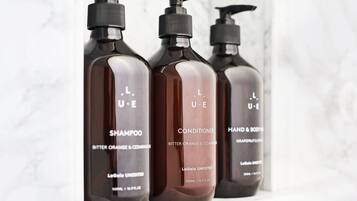 Three bottles of LaGaia Unedited shampoo, conditioner, and hand & body wash on a white surface.