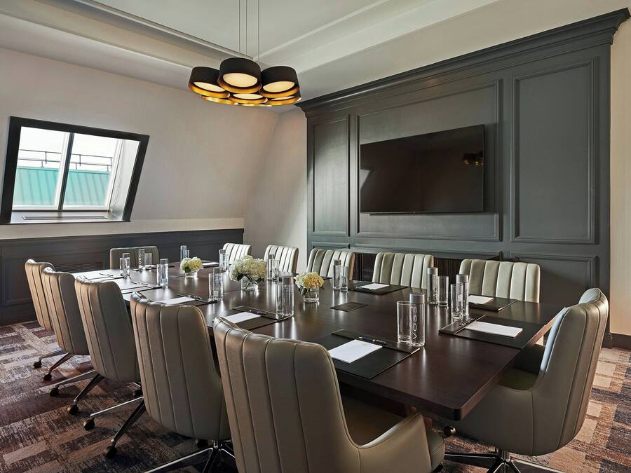 A conference room with a large table, multiple chairs, a television, and a window with a view.