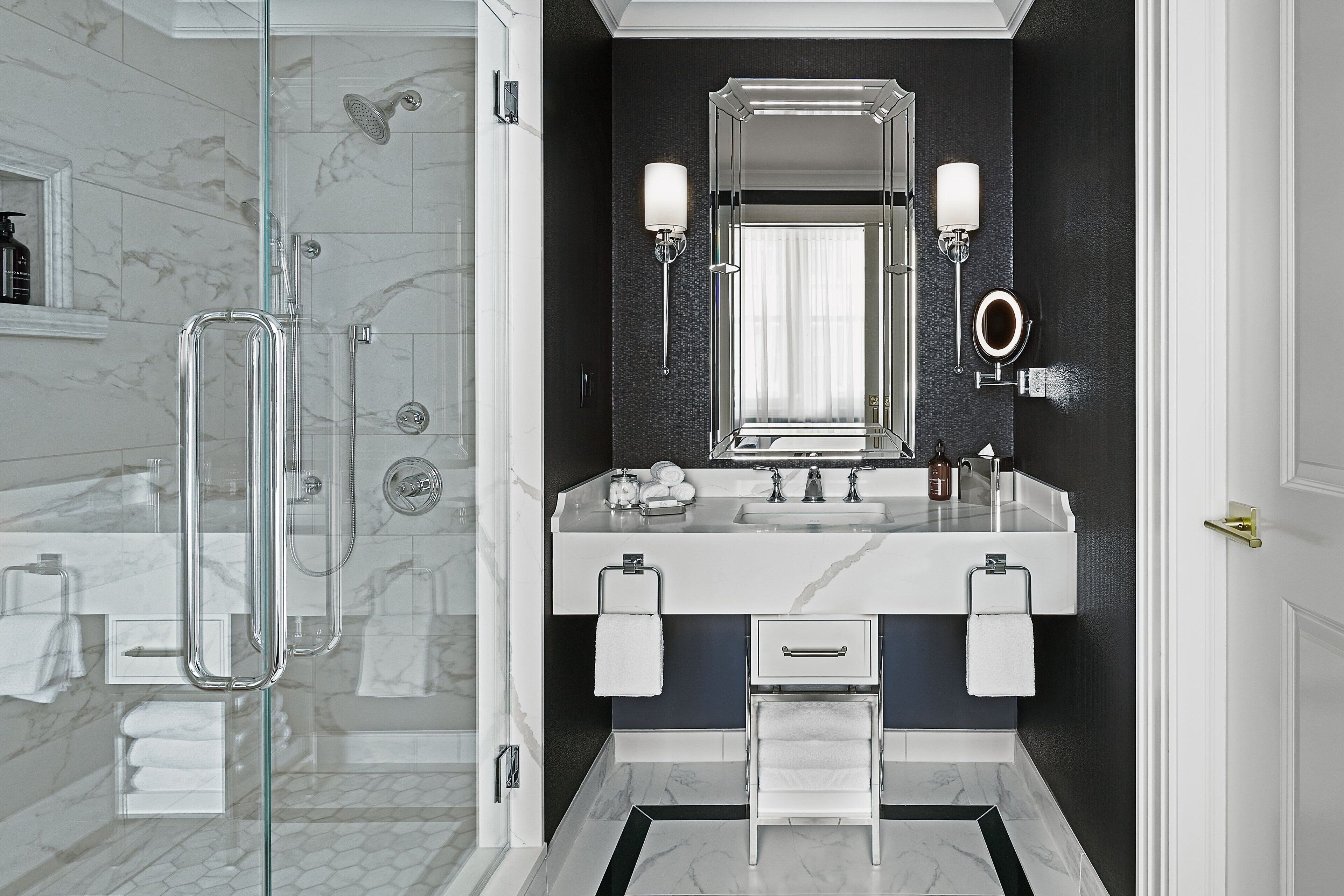 A modern bathroom with a glass-enclosed shower, a large mirror, and a marble-tiled floor.