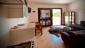 Een moderne keuken met een fornuis, een eettafel met stoelen, een bank en een schuifpui naar een balkon.