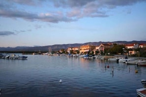A waterfront marina with boats docked, buildings along the shore, and mountains in the background.