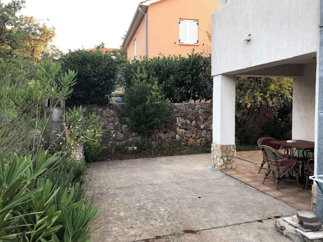 Pihalla on terassialue, jossa on kivimuuri, ulkokalusteita ja taustalla näkyy rakennus.