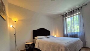 A bedroom with a bed, bedside lamps, a floor lamp, and a window with curtains. - Holiday apartment on the ground floor, with a terrace in Mediterranean greenery and air-conditioned (Klimno)