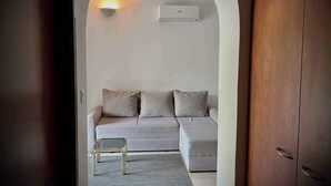 A cozy living room with a sofa and a small table, an air conditioning unit on the wall, and a wooden door. - Holiday apartment on the ground floor, with a terrace in Mediterranean greenery and air-conditioned (Klimno)