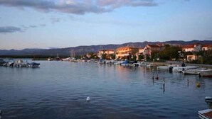 A waterfront marina with boats docked, buildings along the shore, and mountains in the background. - Holiday apartment with terrace overlooking the sea, air-conditioned, on the 1st floor (Klimno)