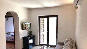 En stue med sofa, TV og en skydedør, der fører ud til en balkon.