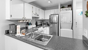 Une cuisine moderne avec des armoires blanches, des appareils en acier inoxydable, un comptoir en granit et un espace buanderie visible.