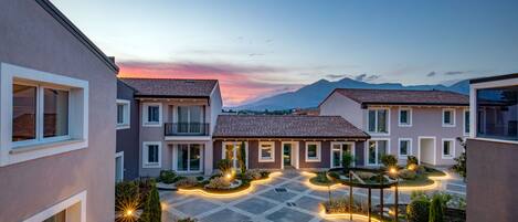 Un complejo residencial con varias casas, un patio con pavimento geométrico y un cielo al atardecer.
