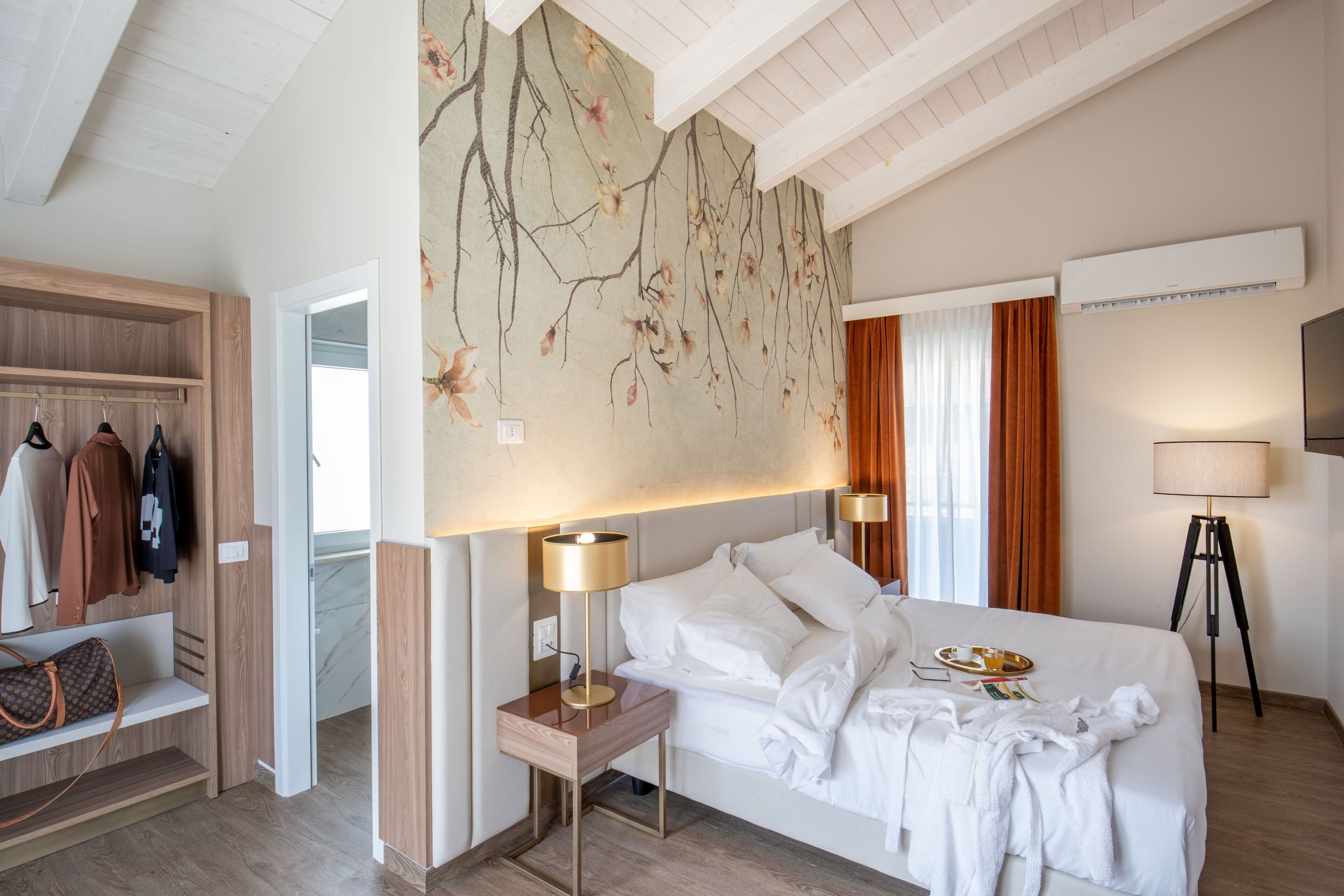 A hotel room with a bed, bedside lamps, a wardrobe, a mirror, and a wall-mounted TV.