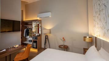 A hotel room with a bed, a desk, a chair, a small table with a vase, a lamp, and a wall-mounted air conditioner.