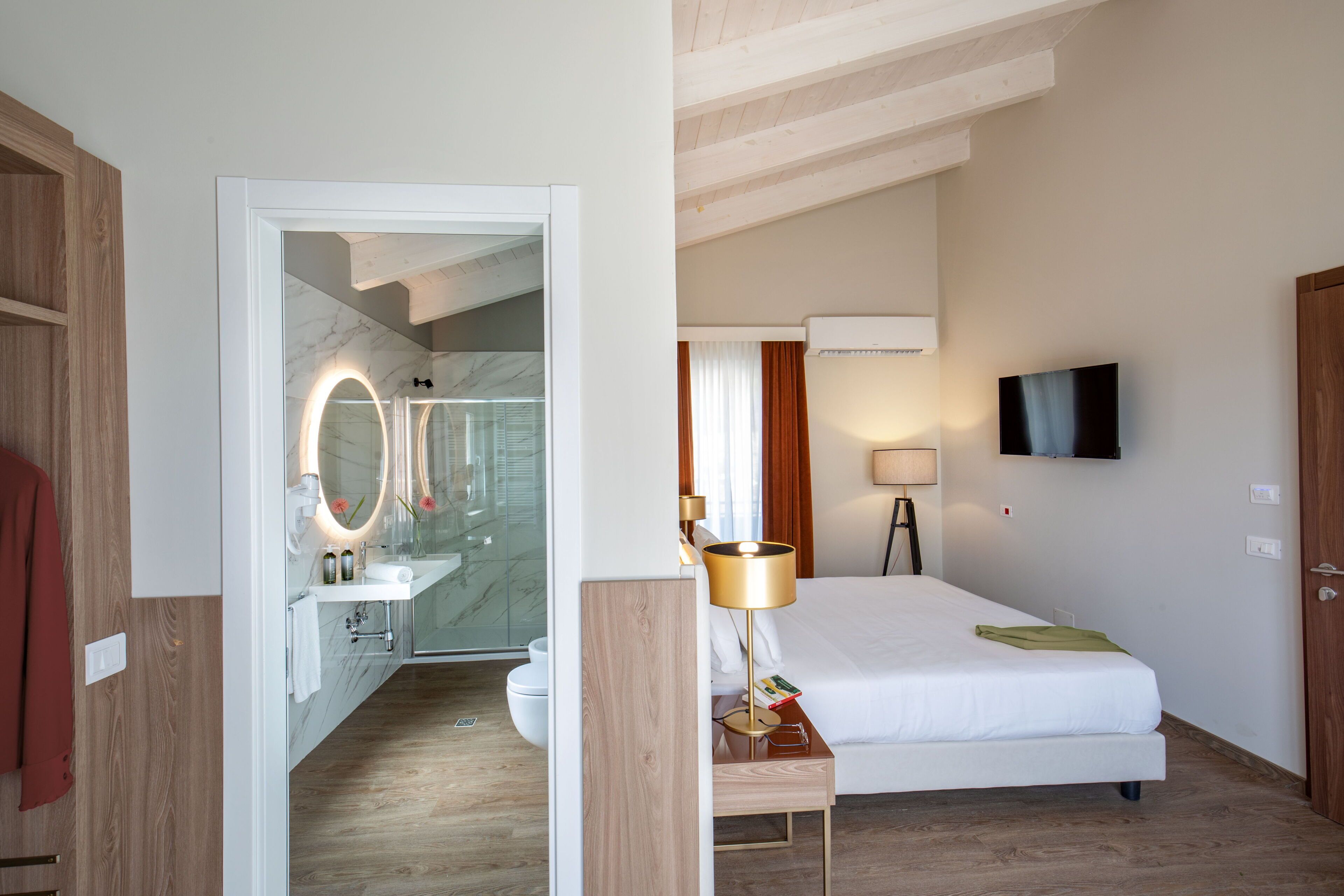 A hotel room with a bed, bedside table, lamp, TV, and a bathroom with a shower and mirror.