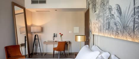 Ein Hotelzimmer mit einem Bett, zwei Stühlen, einem Schreibtisch und einem großen Gemälde an der Wand.