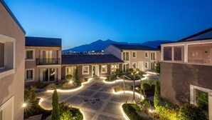 A courtyard with a paved area, surrounded by buildings with balconies and windows, and a mountain in the background.