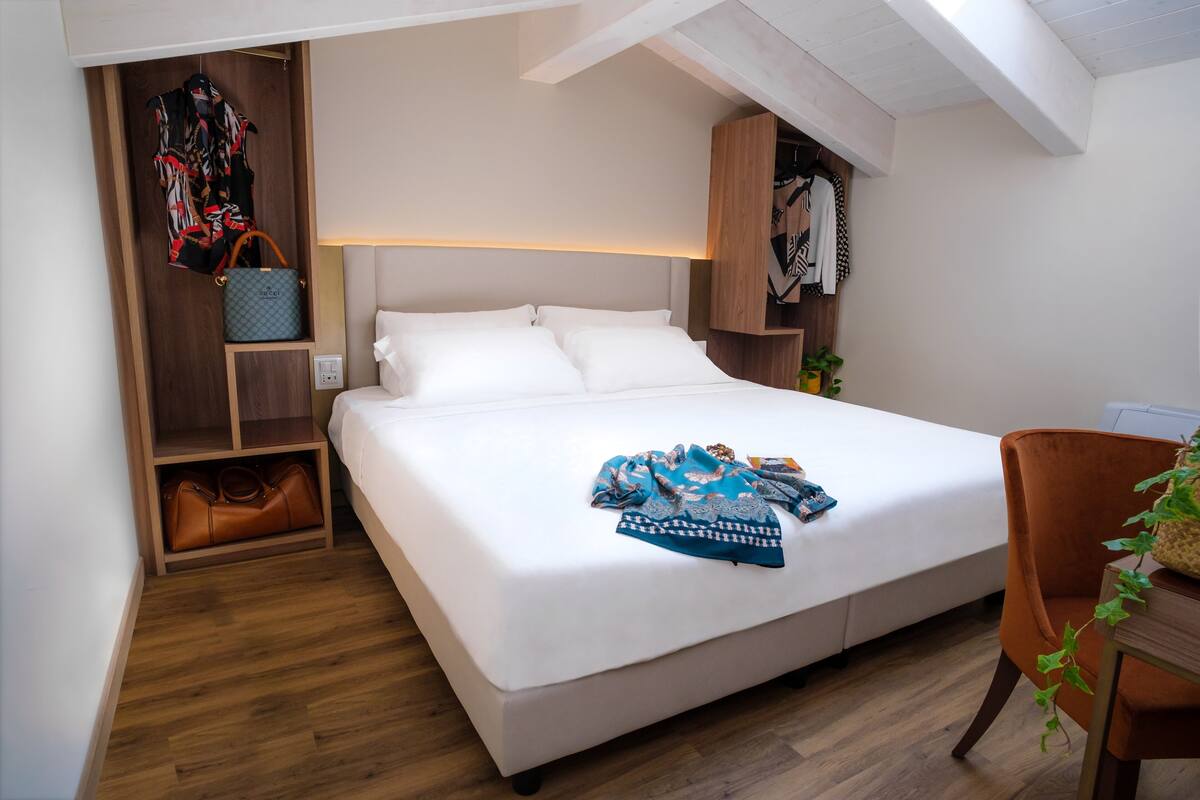 Quarto com cama grande, guarda-roupa de madeira e pequena mesa com planta.