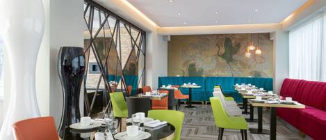 A modern dining area with multiple tables and chairs, a large abstract sculpture, and a mural on the wall.