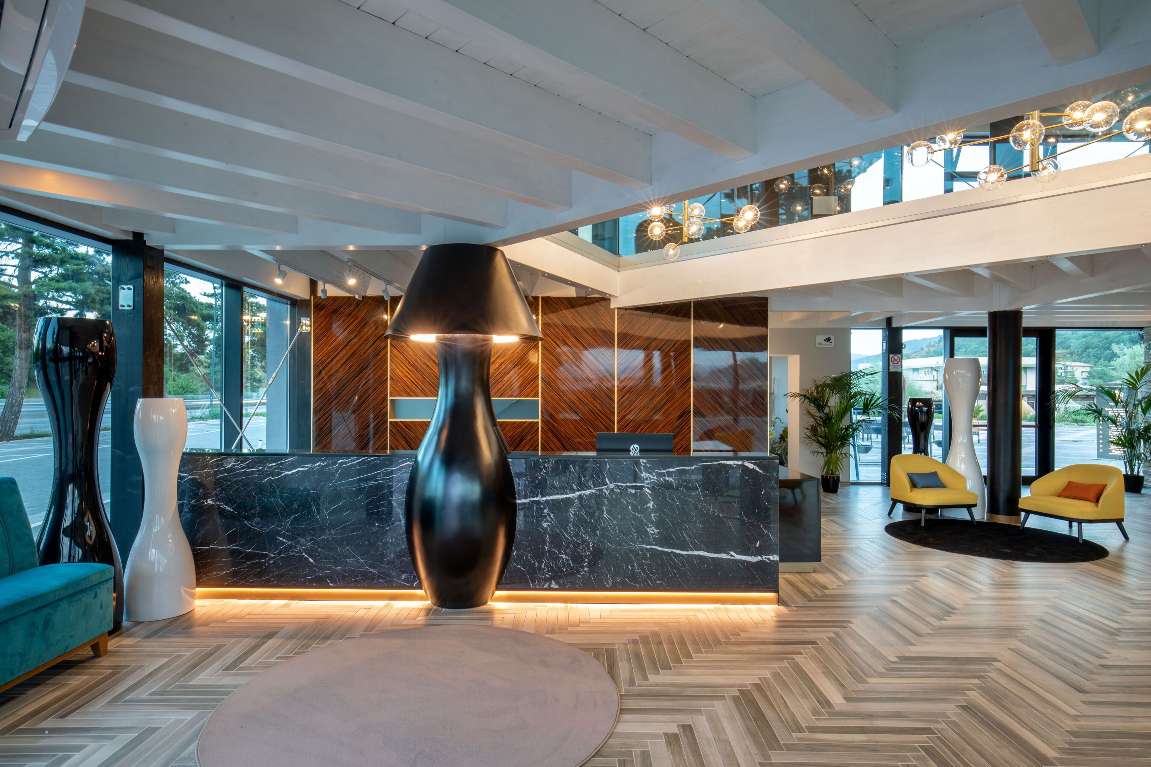 A modern lobby with a marble reception desk, a large black lamp, and yellow chairs.