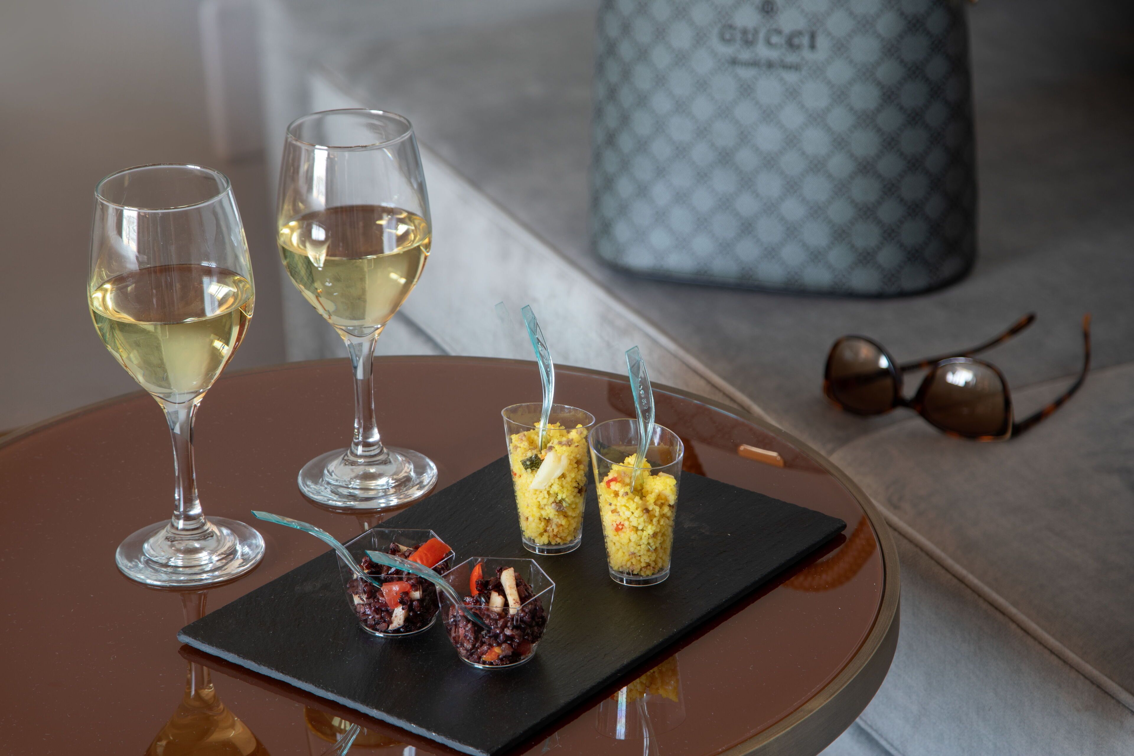 Een tafel met twee wijnglazen, een zwart dienblad met eten en een Gucci tas op de achtergrond.
