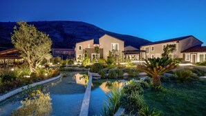 A modern hotel with a pool, landscaped garden, and a mountain backdrop.