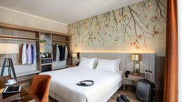 Habitación de hotel con una cama grande, un escritorio con silla, un armario y una lámpara de pared.