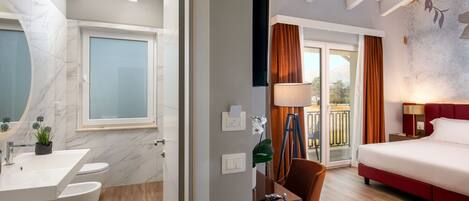 A modern hotel room with a bathroom, a desk, and a bed.