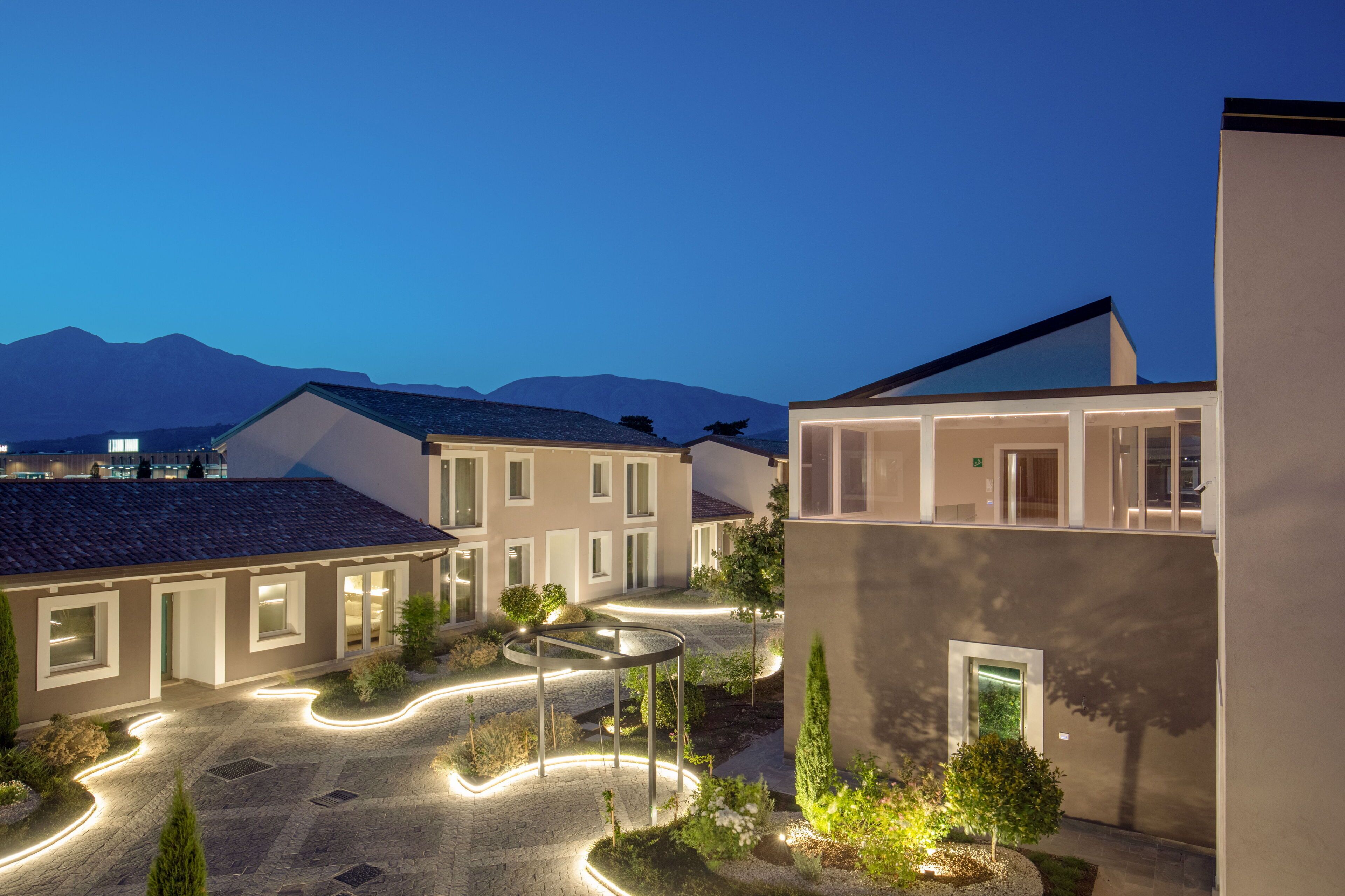 A modern building complex with multiple residential units, a central courtyard, and a mountain backdrop.
