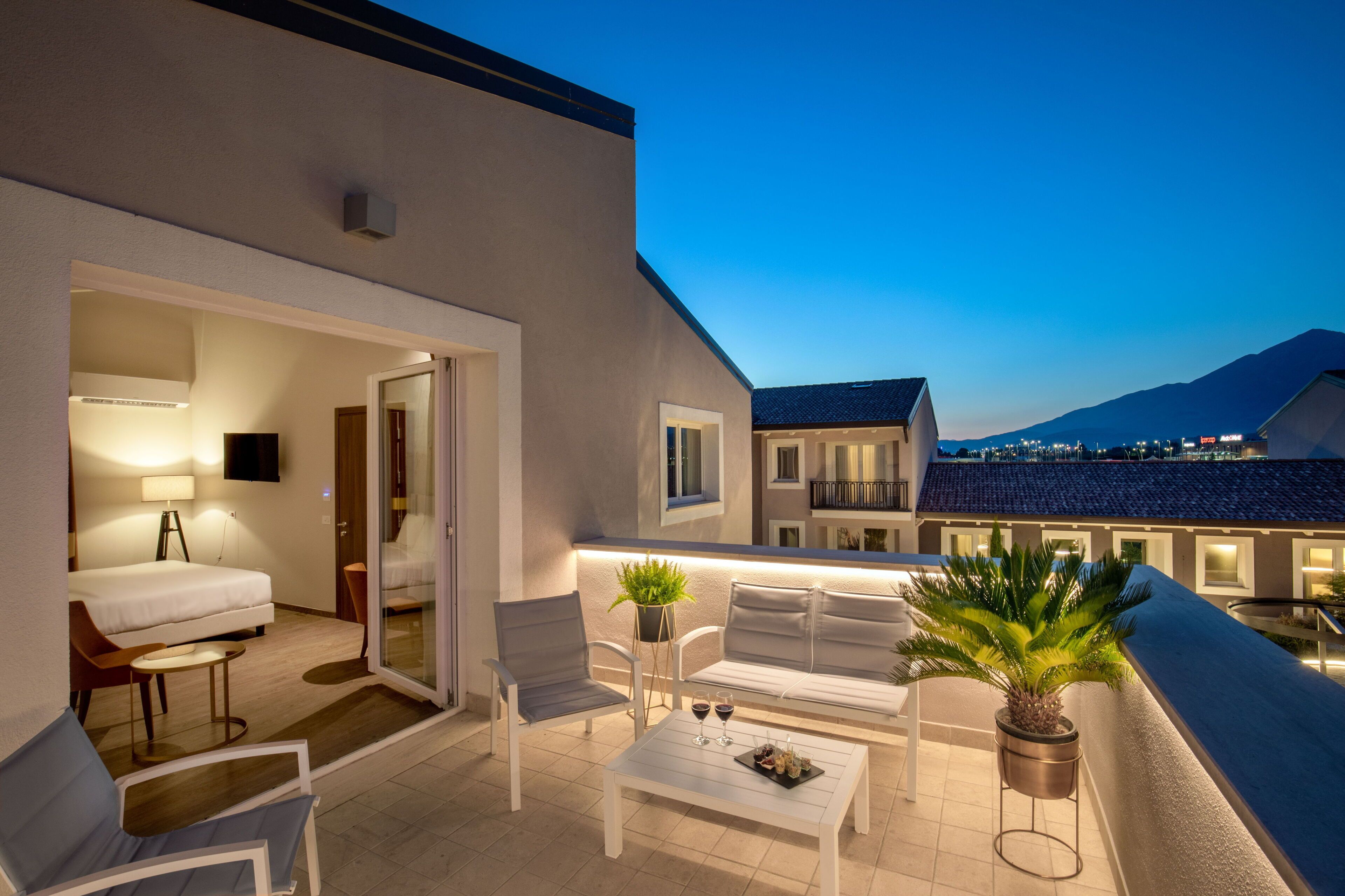 A balcony with white furniture, a potted plant, and a table with wine glasses.