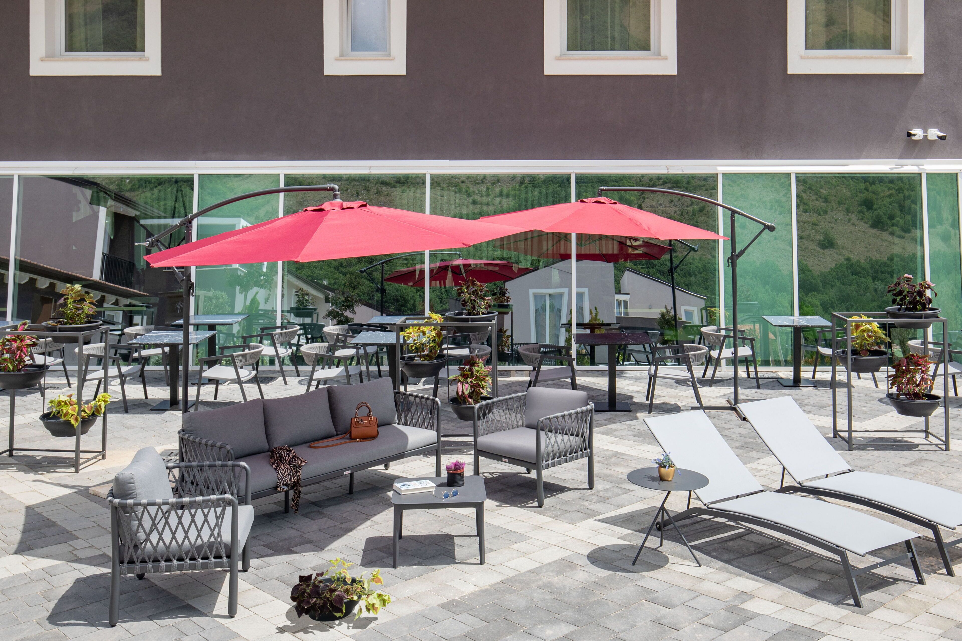 An outdoor patio with seating arrangements, including a sofa, chairs, and lounge chairs, and red umbrellas providing shade.