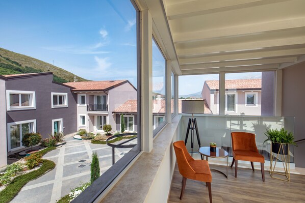A balcony with two orange chairs and a small table, overlooking a courtyard with neatly arranged plants and a paved walkway. - Hotel Della Piana (Avezzano)
