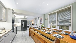 Una cocina moderna con una larga mesa de madera para seis personas, equipada con horno empotrado y refrigerador.