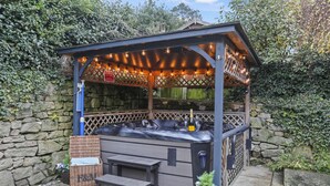 Un jacuzzi con una pérgola de madera encima, una pared de piedra y un banco.