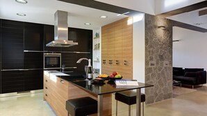 A modern kitchen with a central island, black cabinetry, and a stone accent wall. - Villa Marcelino with Private Pool and free A/C near to Port de Pollensa (Puerto Pollensa)