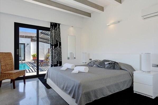 Une chambre moderne avec un grand lit, une chaise, une table de chevet et une vue sur un espace extérieur avec piscine.