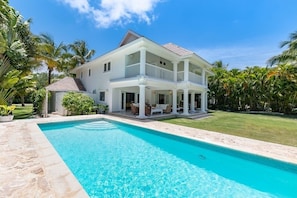 A two-story house with a swimming pool, surrounded by palm trees and a well-maintained lawn.