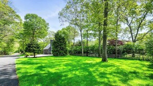 A well-maintained lawn with a variety of trees and a small building, likely a house, surrounded by a fence. - BlackBerry Private home with jacuzzi yearlong (East Hampton)