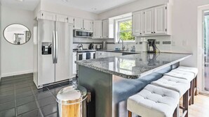A modern kitchen with white cabinets, a large island with bar stools, and a view of the outdoors. - BlackBerry Private home with jacuzzi yearlong (East Hampton)