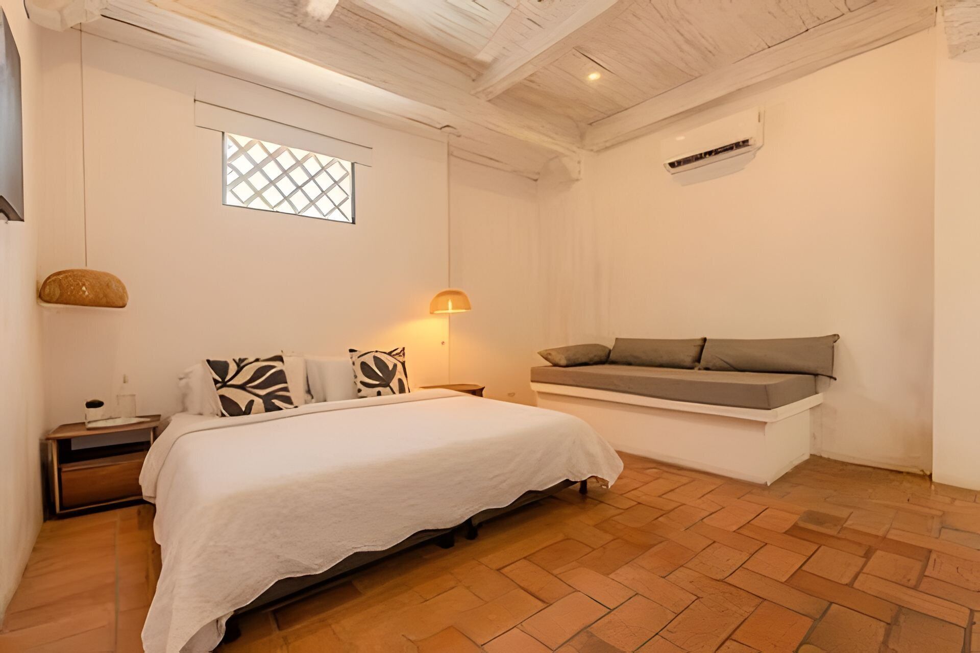 A bedroom with a bed, bedside table, lamp, and a bench with cushions.