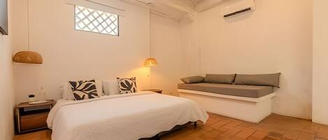 A bedroom with a bed, bedside table, lamp, and a bench with cushions.