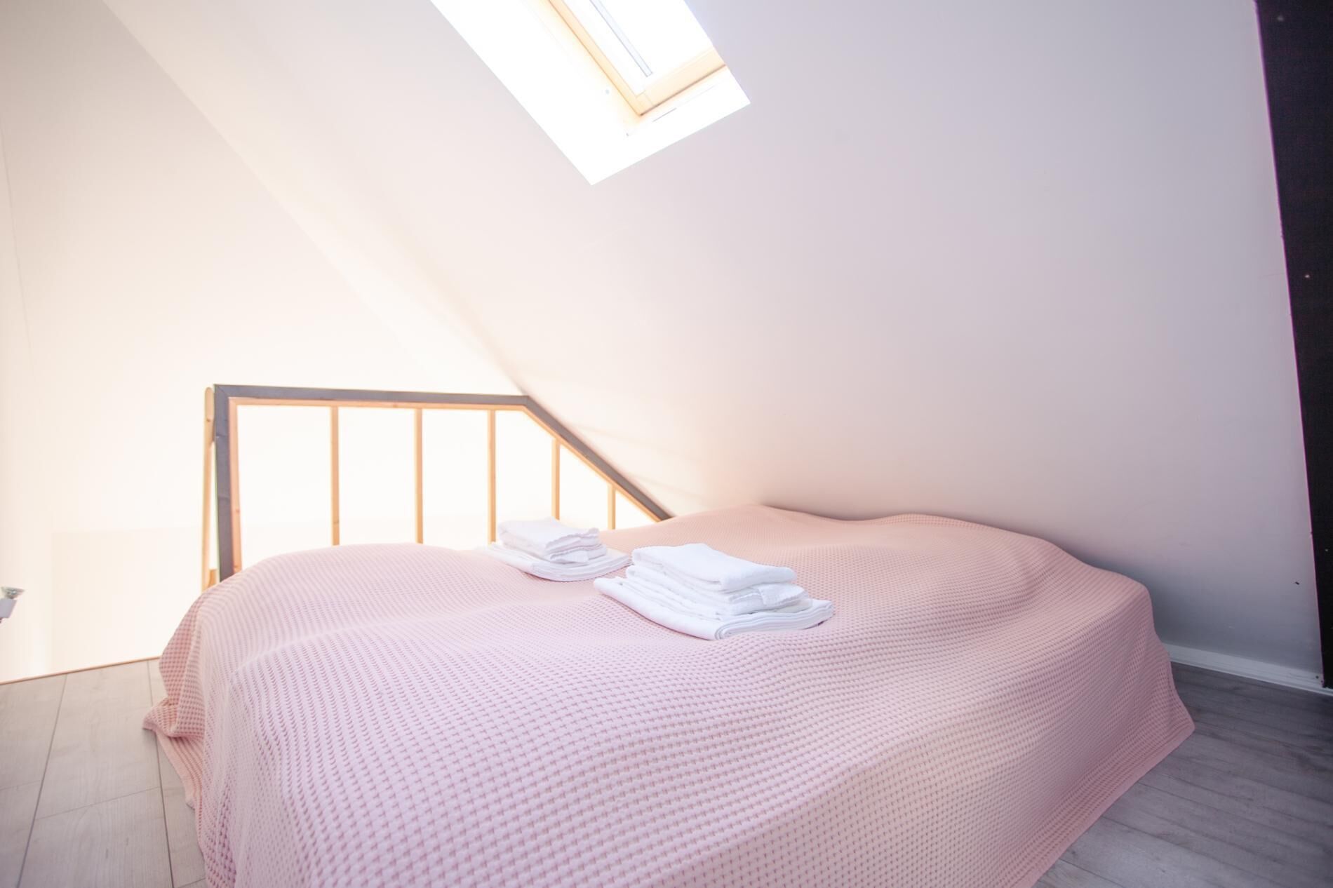 A bedroom with a sloped ceiling, a bed with a pink blanket, and a window providing natural light.