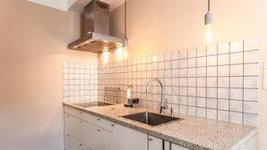 Une cuisine moderne dotée d’un évier en acier inoxydable, d’un plan de travail en granit, de meubles blancs et d’un dosseret carrelé.