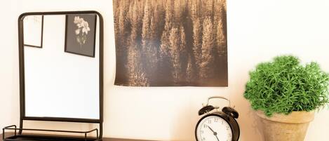 A desk with a black alarm clock, a potted plant, and a framed picture on the wall.