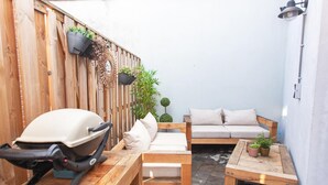 Une petite terrasse avec une table en bois, un barbecue, un canapé et une petite table agrémentée de plantes en pot.