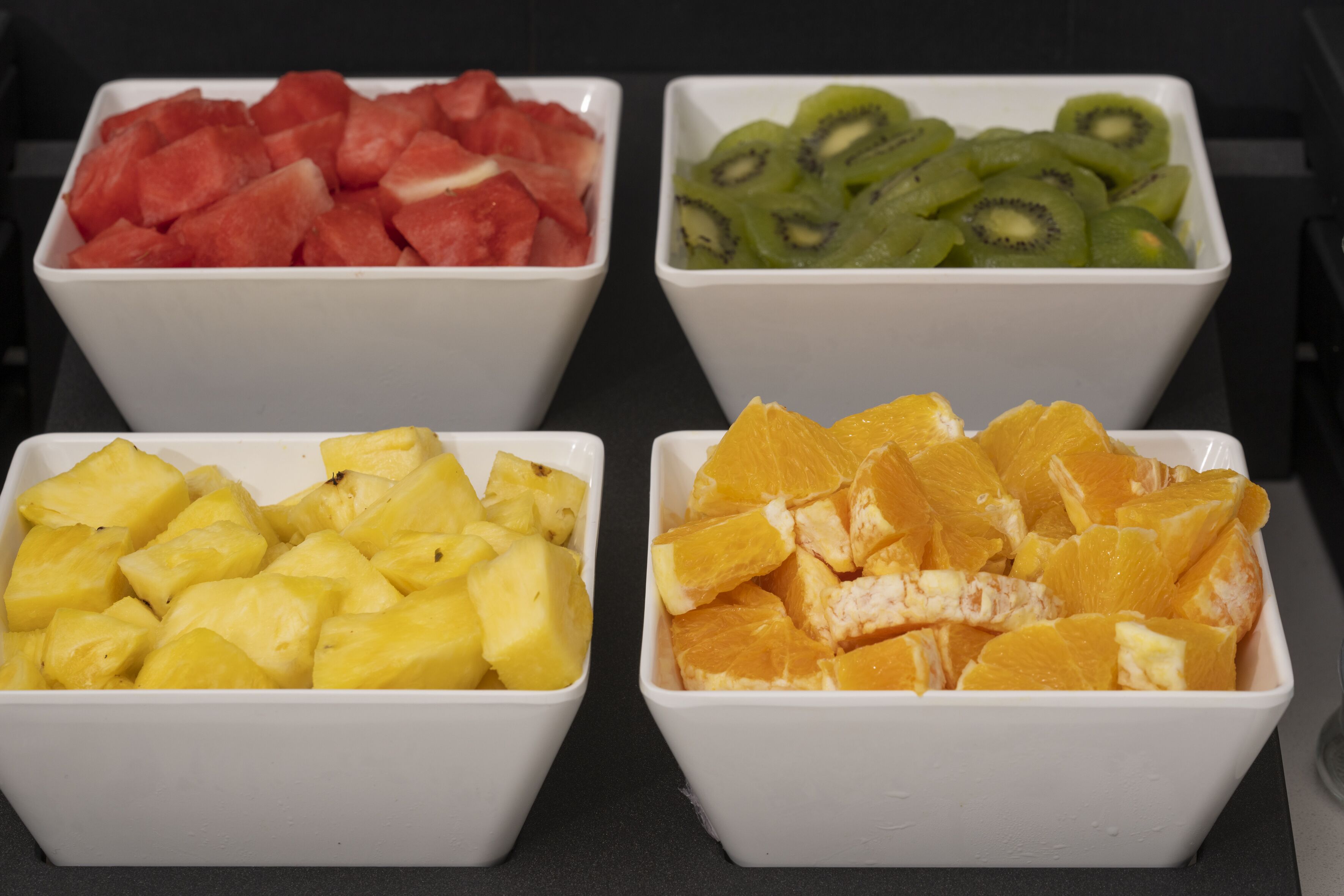 Four white bowls containing different fruits: watermelon, kiwi, pineapple, and orange.