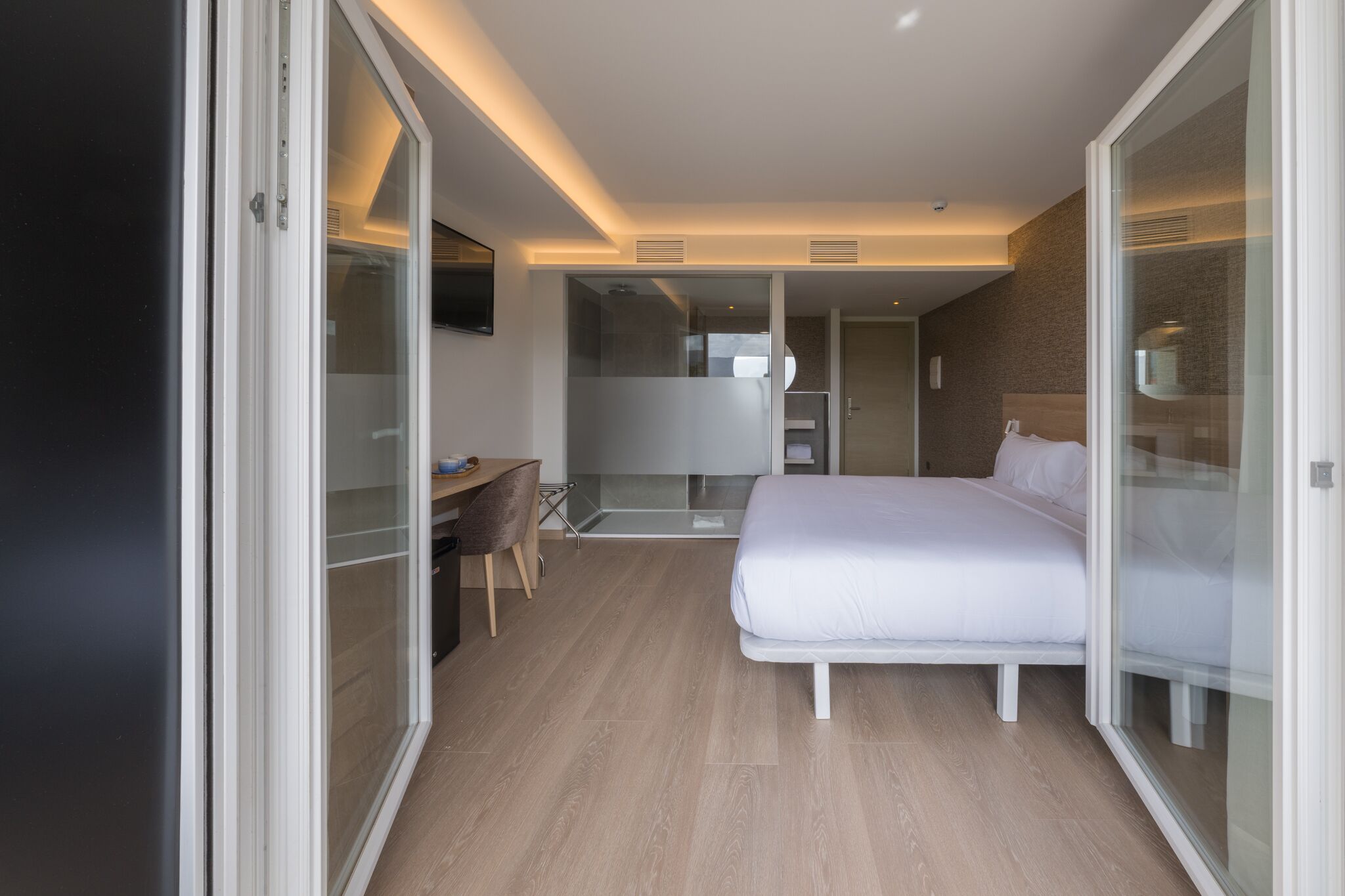 A modern hotel room with a bed, desk, and sliding glass doors.