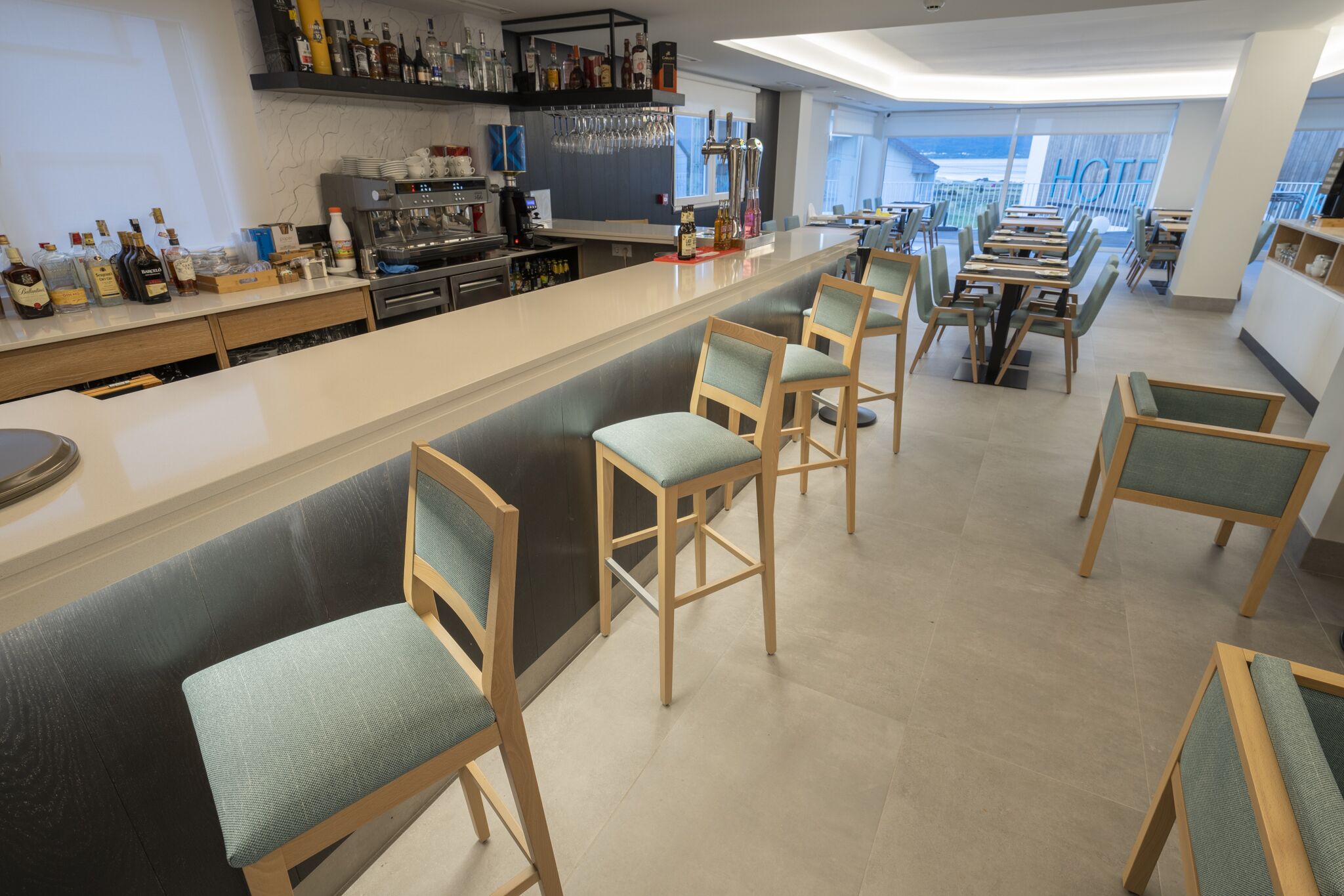 A modern bar area with a long counter, bar stools, and a variety of liquor bottles.
